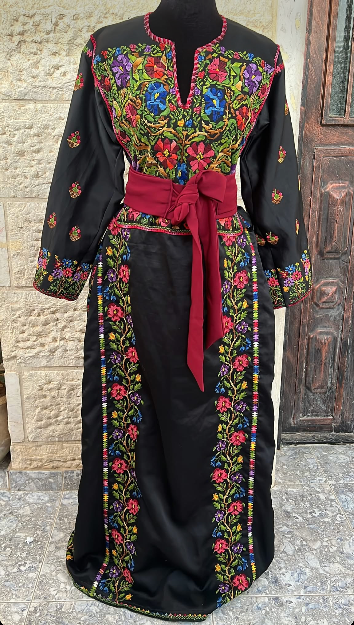 Black embroidered dress with colorful patterns on a mannequin against a textured wall.